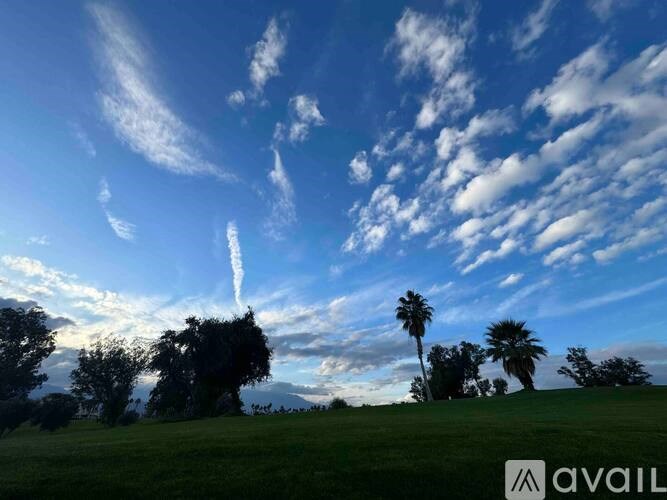 A clear sky with a few clouds and palm trees in the distance.