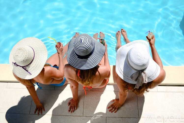 Three women wearing hats are sitting by a pool.