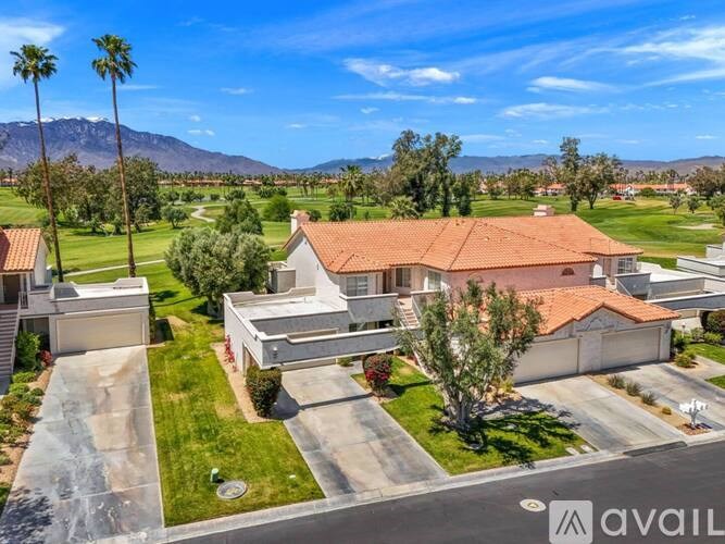 A house with a red roof is surrounded by a green lawn and palm trees.