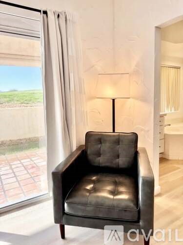 A black leather chair is in front of a window with a lamp on a side table.