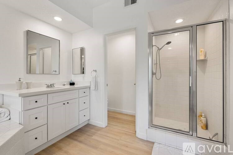 A bathroom with a white cabinet, sink, mirror, and shower.