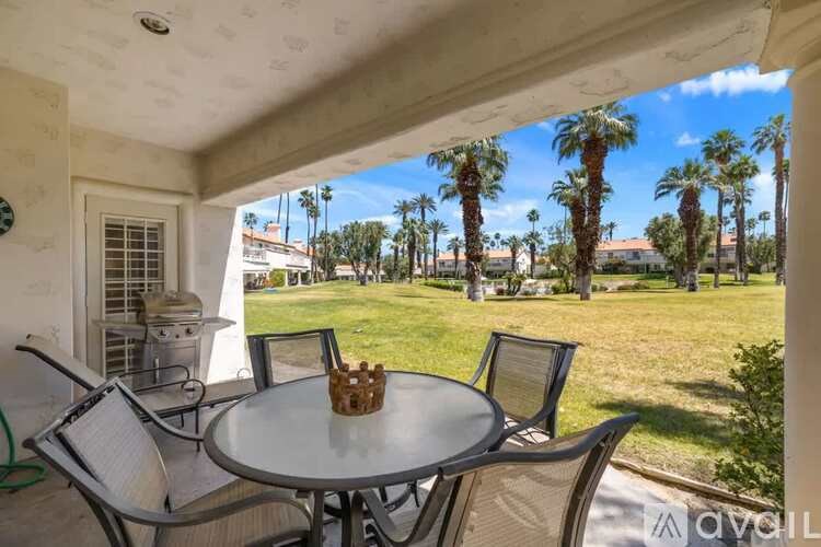 A patio with a table and chairs overlooking a lawn with palm trees.