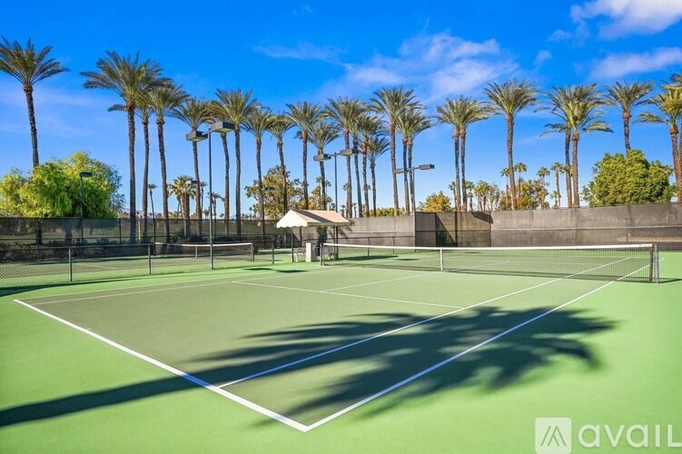 A tennis court surrounded by palm trees under a clear blue sky.