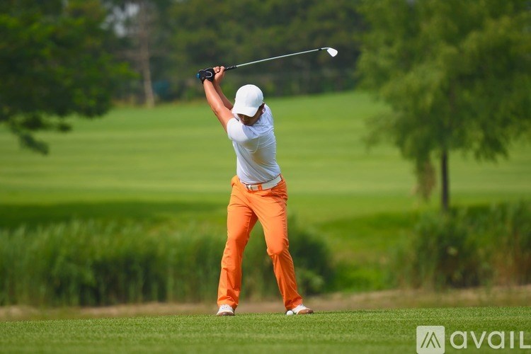 A golfer in a white shirt and orange pants is in the middle of a swing.