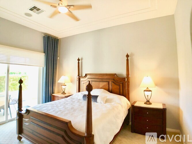 A well-lit bedroom with a large bed, a ceiling fan, and two lamps.