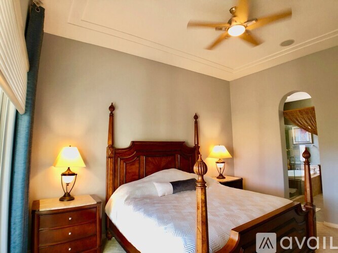 A bedroom with a large bed, two lamps, and a ceiling fan.