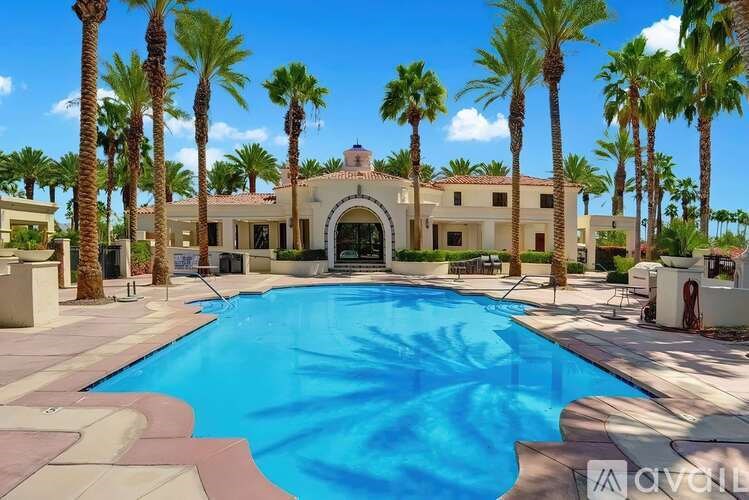 A large swimming pool surrounded by palm trees and a building in the background.