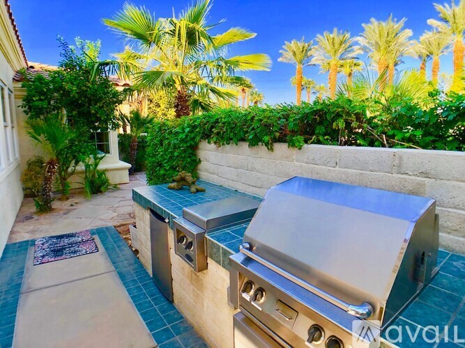 A BBQ grill is on a patio with a wall of green plants behind it.