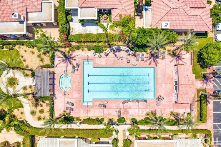 An aerial view of a swimming pool surrounded by palm trees and a few buildings.