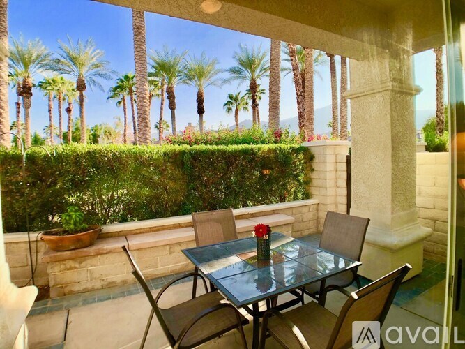 A table with chairs is set up on a patio with a view of palm trees.