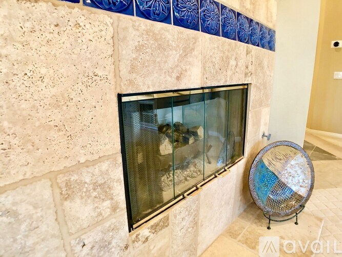 A fireplace with a blue tile border and a fan on the floor.