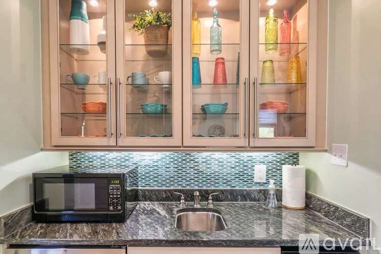 A kitchen with a black microwave, sink, and cabinets with glass doors.