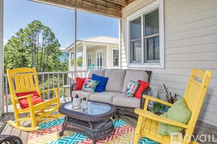 A balcony with a yellow chair and a glass table with a bottle on it.