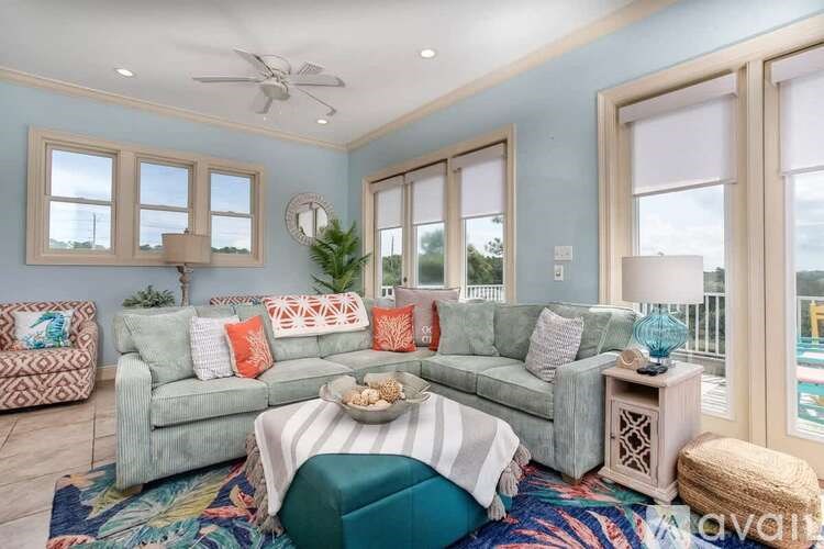 A living room with a grey couch, a round ottoman, and a rug with a pattern.