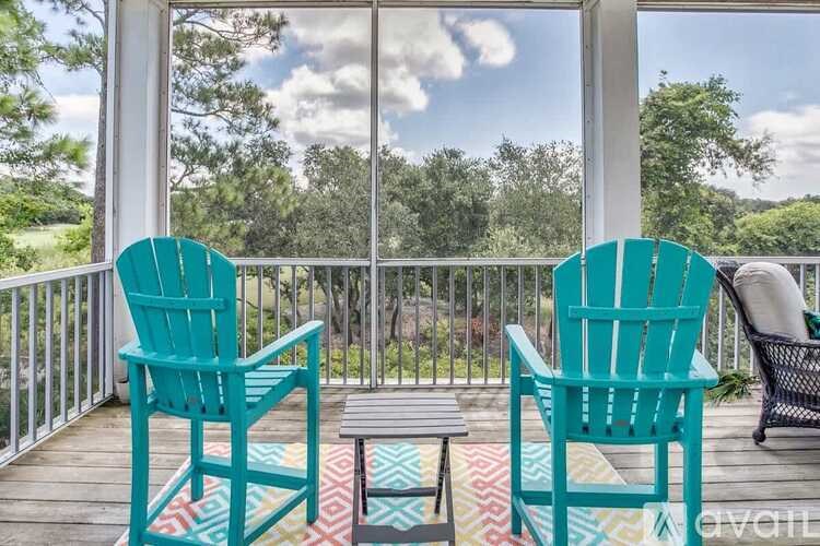 Two chairs and a table on a deck with a view of the trees.
