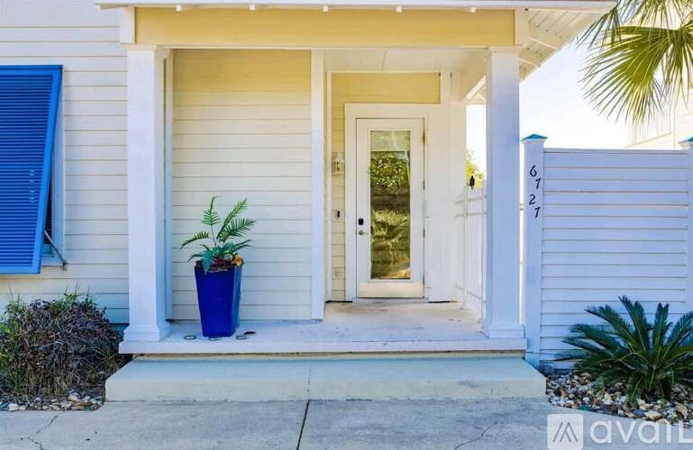 A white house with a blue door and a blue pot with a plant in front of it.