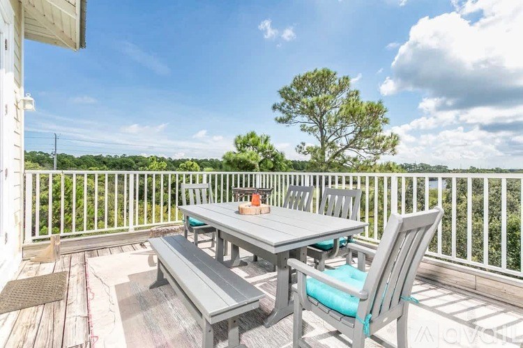 A wooden table with four chairs is set on a deck with a view of trees.