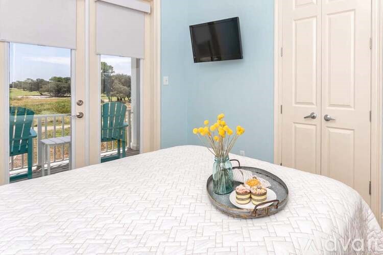 A bedroom with a bed, a tray with cookies and flowers, and a flat screen TV mounted on the wall.