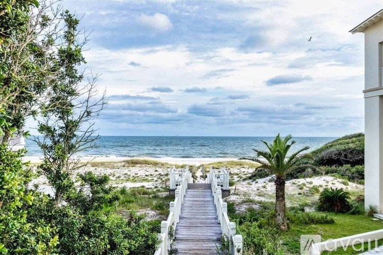 A wooden walkway leads to a beach with a white building on the right.