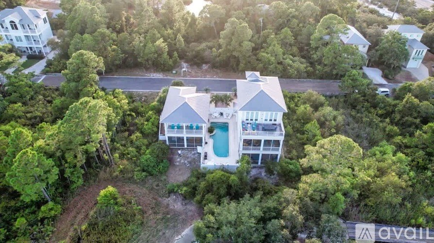 A large house with a pool is surrounded by trees and has a "For Sale" sign.