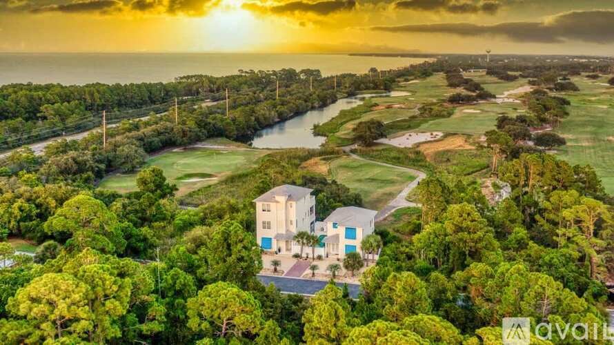 A house is surrounded by greenery and a river under a cloudy sky.