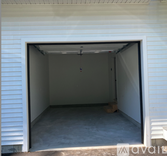 A white garage door is open, revealing a concrete floor and a wall with a small window.