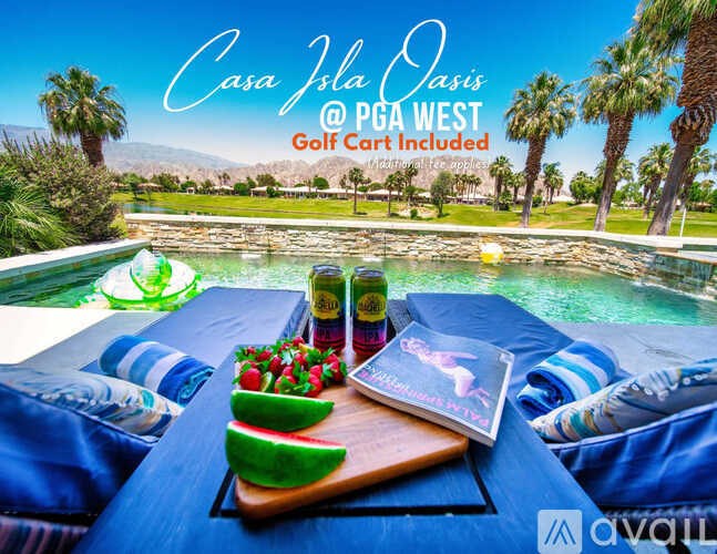 A poolside table with a book, a bottle, and a plate of fruit.