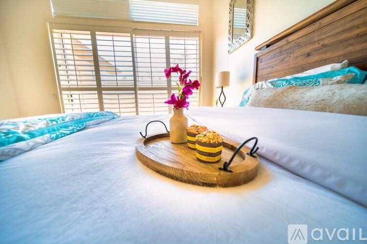 A wooden tray with a flower, sunglasses, and macarons on a bed.