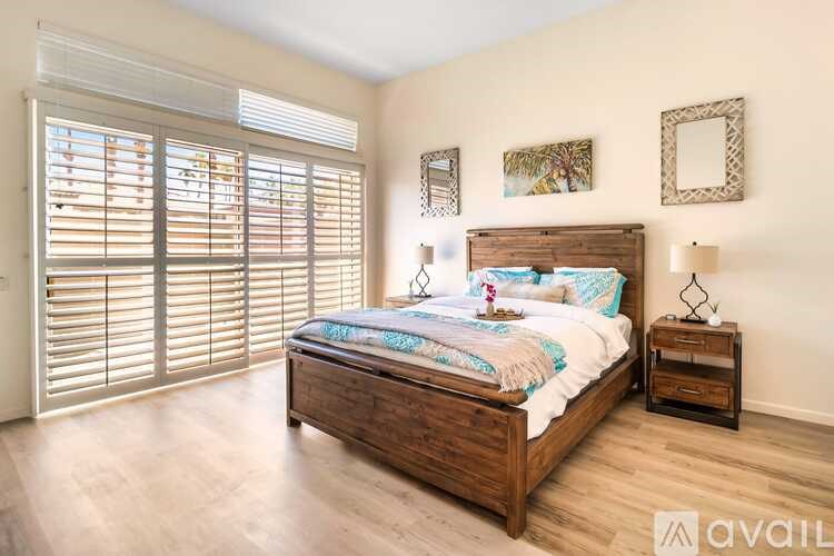 A bedroom with a large bed, wooden nightstand, and a window with blinds.