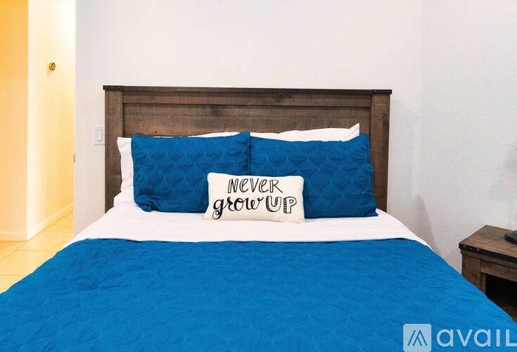 A bed with a blue comforter and a pillow that says "never grow up".