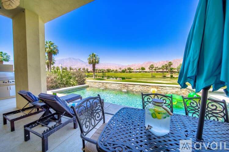 A table with a glass of lemonade sits on a patio overlooking a pool and a mountain.