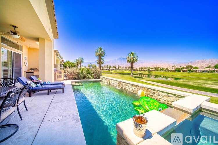 A pool with a glass table and chairs is surrounded by a desert landscape.