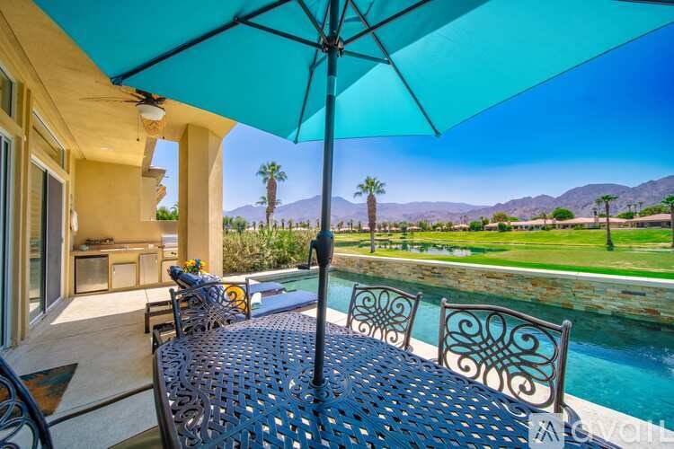 A patio with a table and chairs overlooking a pool and a mountain.