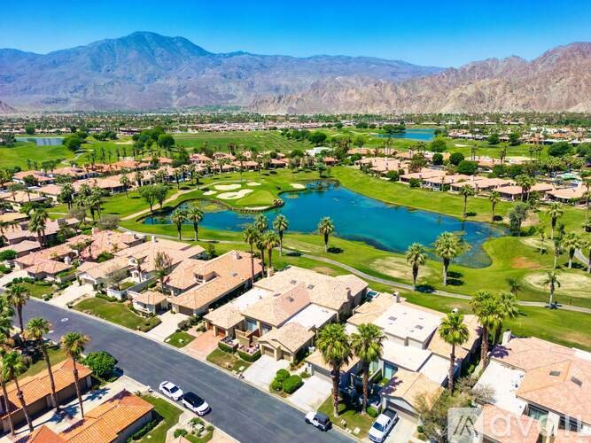 A bird's eye view of a residential area with houses, palm trees, and a lake.