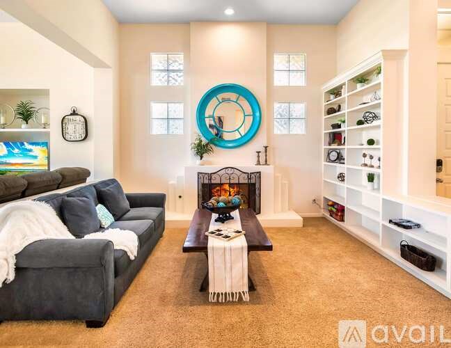 A living room with a grey couch, a fireplace, and a large blue circular mirror on the wall.