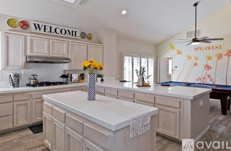 A kitchen with a white countertop and cabinets, a "Welcome" sign, and a "#PGAWEST" sign on the wall.