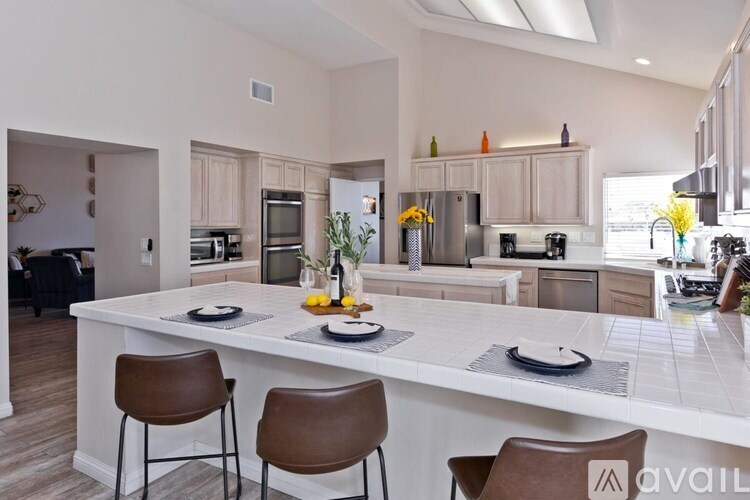 A modern kitchen with a white island and brown chairs.