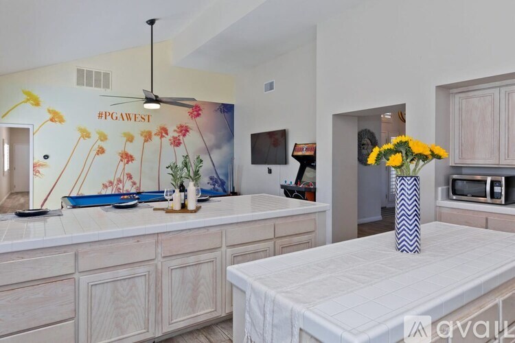 A bedroom with a bed, a fan, and a painting on the wall.