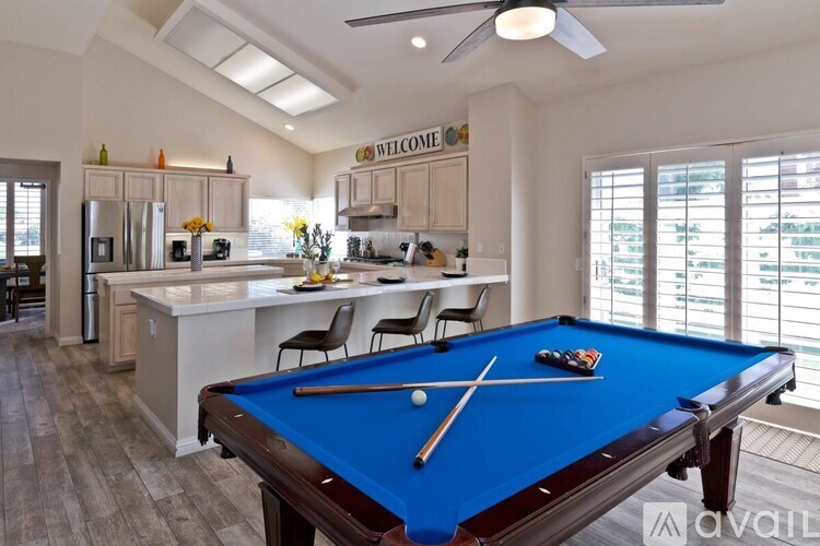 A pool table is in the middle of a kitchen and dining area.