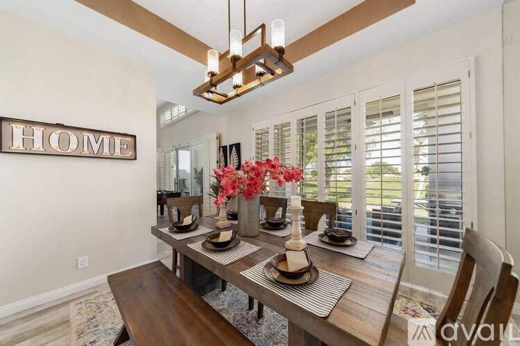 A dining room with a wooden table and chairs, a hanging light fixture, and a "HOME" sign on the wall.