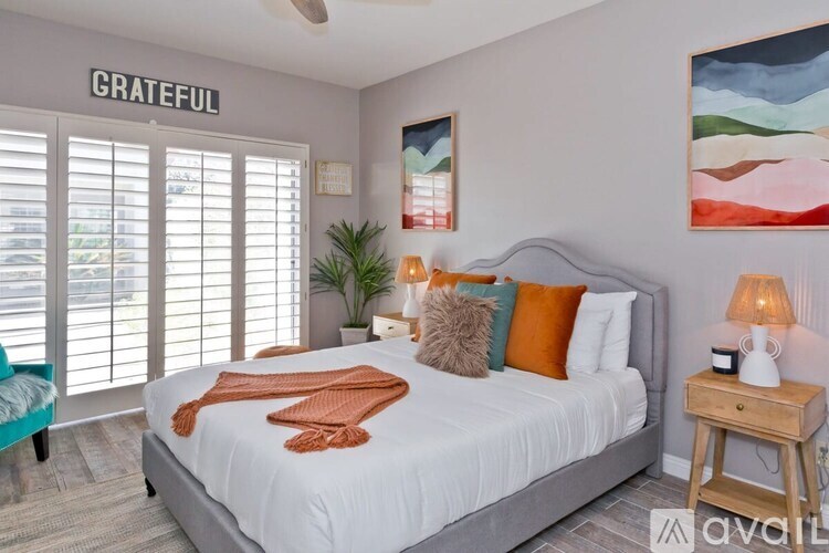 A bedroom with a bed, a table with a lamp, and a painting on the wall.
