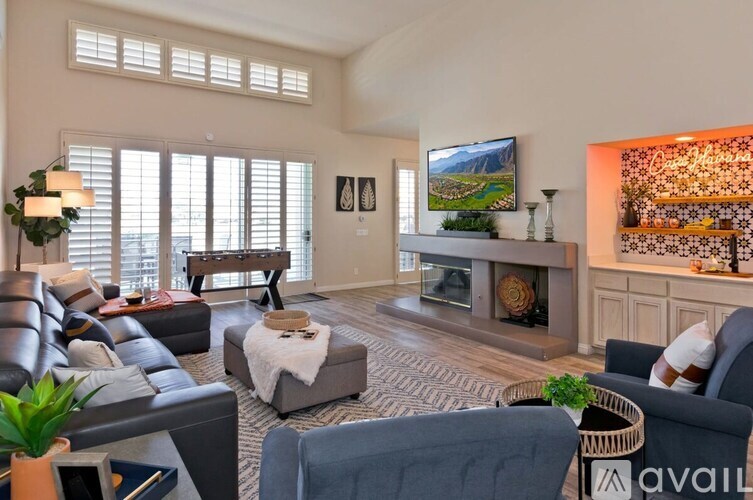 A living room with a grey sofa, a black leather couch, a wooden coffee table, a TV, a fireplace, and a painting on the wall.