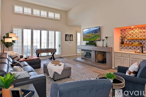 A living room with a grey sofa, a black leather couch, a wooden coffee table, a TV, a fireplace, and a painting on the wall.