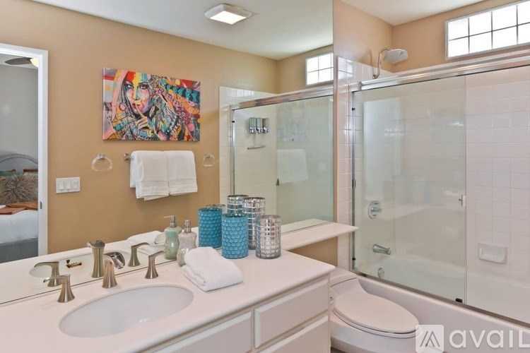 A bathroom with a white sink and toilet, a glass shower stall, and a painting on the wall.