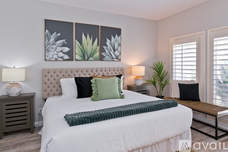 A bedroom with a large bed, a bench, and a painting of three plants on the wall.