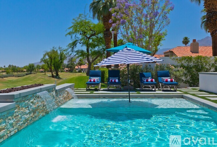 A pool with a striped umbrella and two chairs.