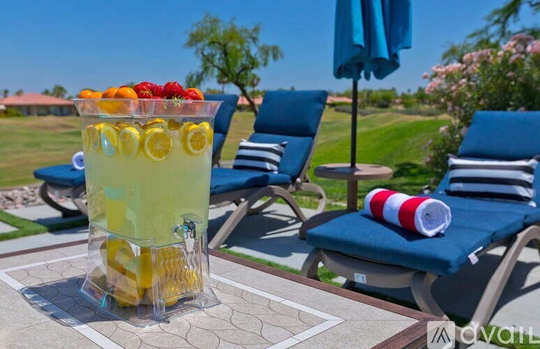 A glass of lemonade with slices of lemon and raspberries on a table outside.