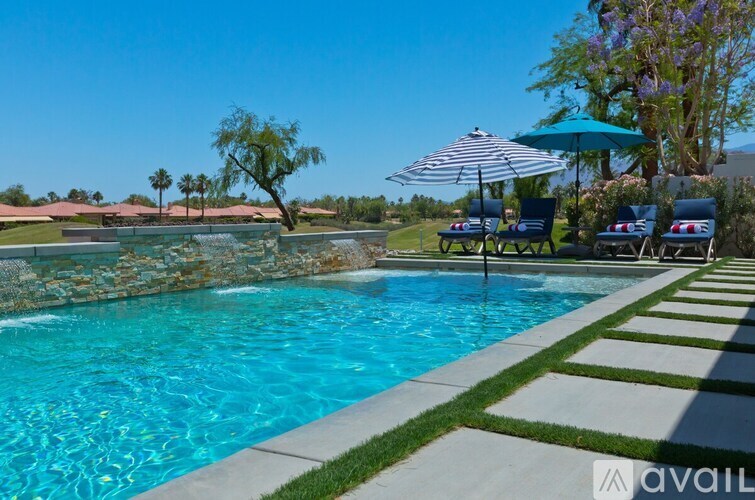 A pool with a stone wall and a lawn with chairs and umbrellas.