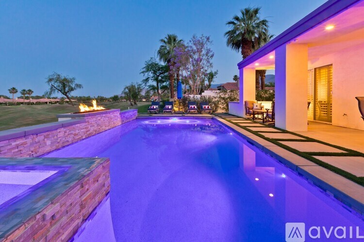 A pool with a lit up wall and a house in the background.