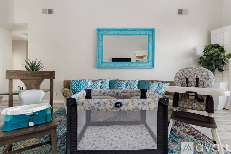 A baby crib sits in a living room with a mirror and a potted plant.